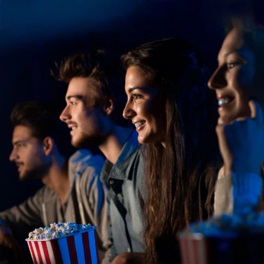Amigos sonriendo en el cine mientras comen palomitas de maíz