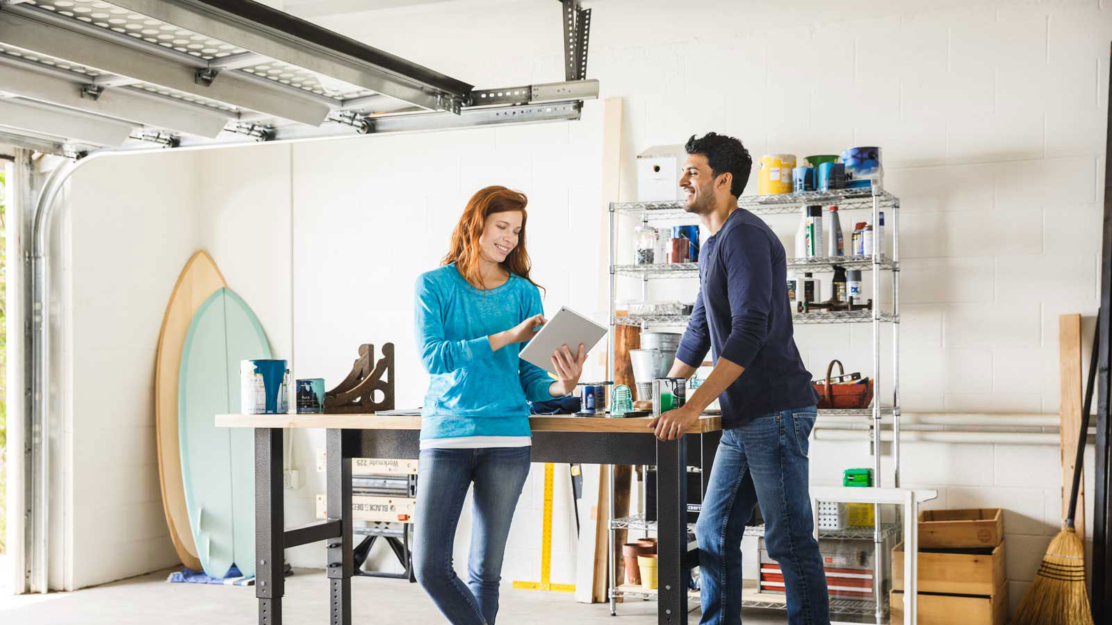 Happy man and woman talking while standing in a home garage and looking at a tablet. Happy man and woman talking while standing in a home garage and looking at a tablet.