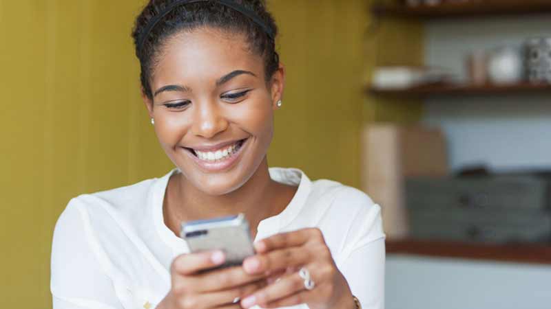 A smiling woman looks at her phone.